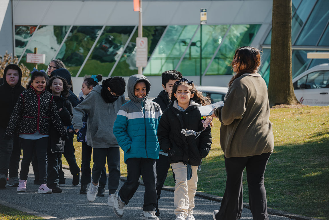 A group of smiling elementary school children in winter coats walk across the Muhlenberg campus